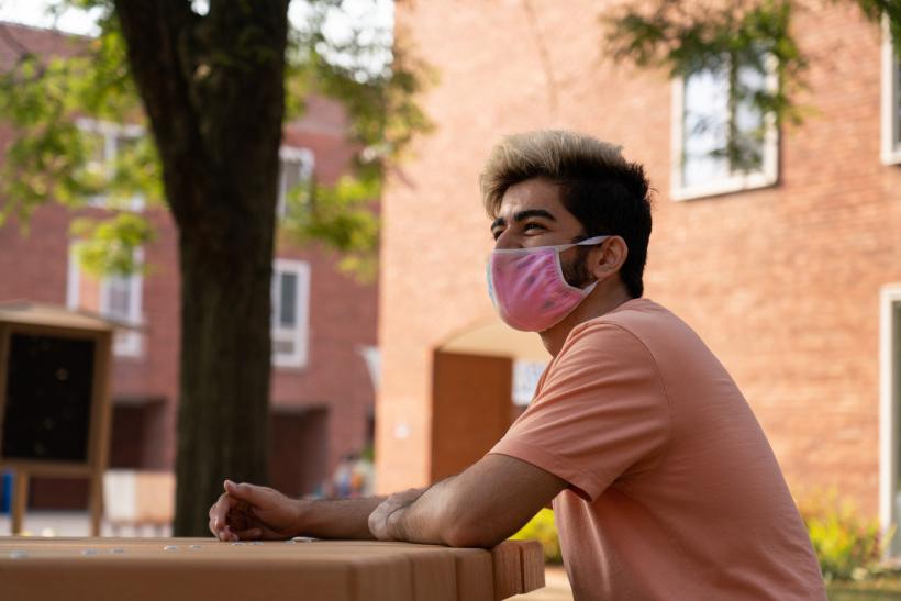 A student sitting outside the '64 Halls, wearing a mask.